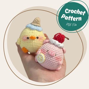 May include: Two handmade crochet amigurumi figures: a yellow chick with a blue and tan hat and an orange beak, and a pink pig with a cherry on its head and a lemon slice. The image includes a green circle with the text "Crochet Pattern PDF File".