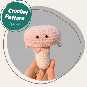 May include: A pink crocheted mushroom amigurumi toy with black eyes and pearl earrings. The mushroom has a white bow tied around the stem.