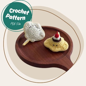 May include: Two crocheted items sit on a wooden tray. One is a white, fan-shaped design. The other is a yellow, hat-shaped design with a cherry on top. A teal circle with the words "Crochet Pattern PDF File" is in the upper left corner.