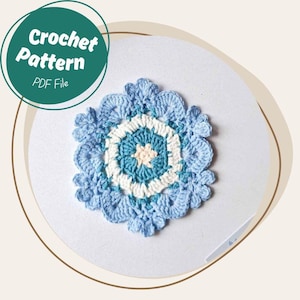 May include: A blue and white crocheted doily with a floral design. The doily has a central star shape and is surrounded by a scalloped edge. The image also includes a green circle with the text "Crochet Pattern PDF File".