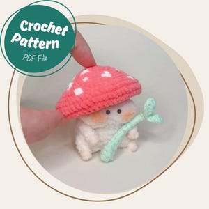 May include: A crocheted mushroom figure with a red cap dotted with white spots. The mushroom has a white body, small black eyes, and a light green stem. The image includes text that says "Crochet Pattern PDF File".