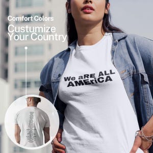 Puede incluir: Una camiseta blanca con el texto "We ARE ALL AMERICA" en negro. La modelo lleva una chaqueta vaquera. La imagen también incluye el texto "Comfort Colors" y "Customize Your Country".