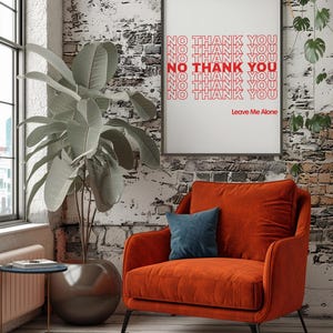 May include: An orange armchair with a blue pillow sits in front of a brick wall. A framed print displays the words "NO THANK YOU" in red, with "Leave Me Alone" below. A large potted plant is to the left.