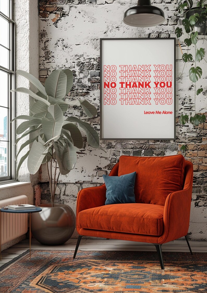 May include: An orange armchair with a blue pillow sits in front of a brick wall. A framed print displays the words "NO THANK YOU" in red, with "Leave Me Alone" below. A large potted plant is to the left.