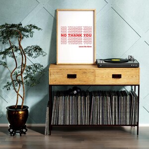 May include: A framed print with the text "NO THANK YOU" in red, displayed on a wooden console with a record player. The console also holds a collection of vinyl records. A potted bonsai tree is on the left.
