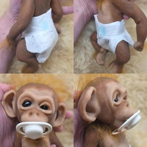 May include: A realistic monkey doll with brown skin, orange hair, and large ears. The doll wears a white diaper and has a white pacifier in its mouth. The figure is shown from multiple angles, displaying its textured skin, facial features, and limbs.