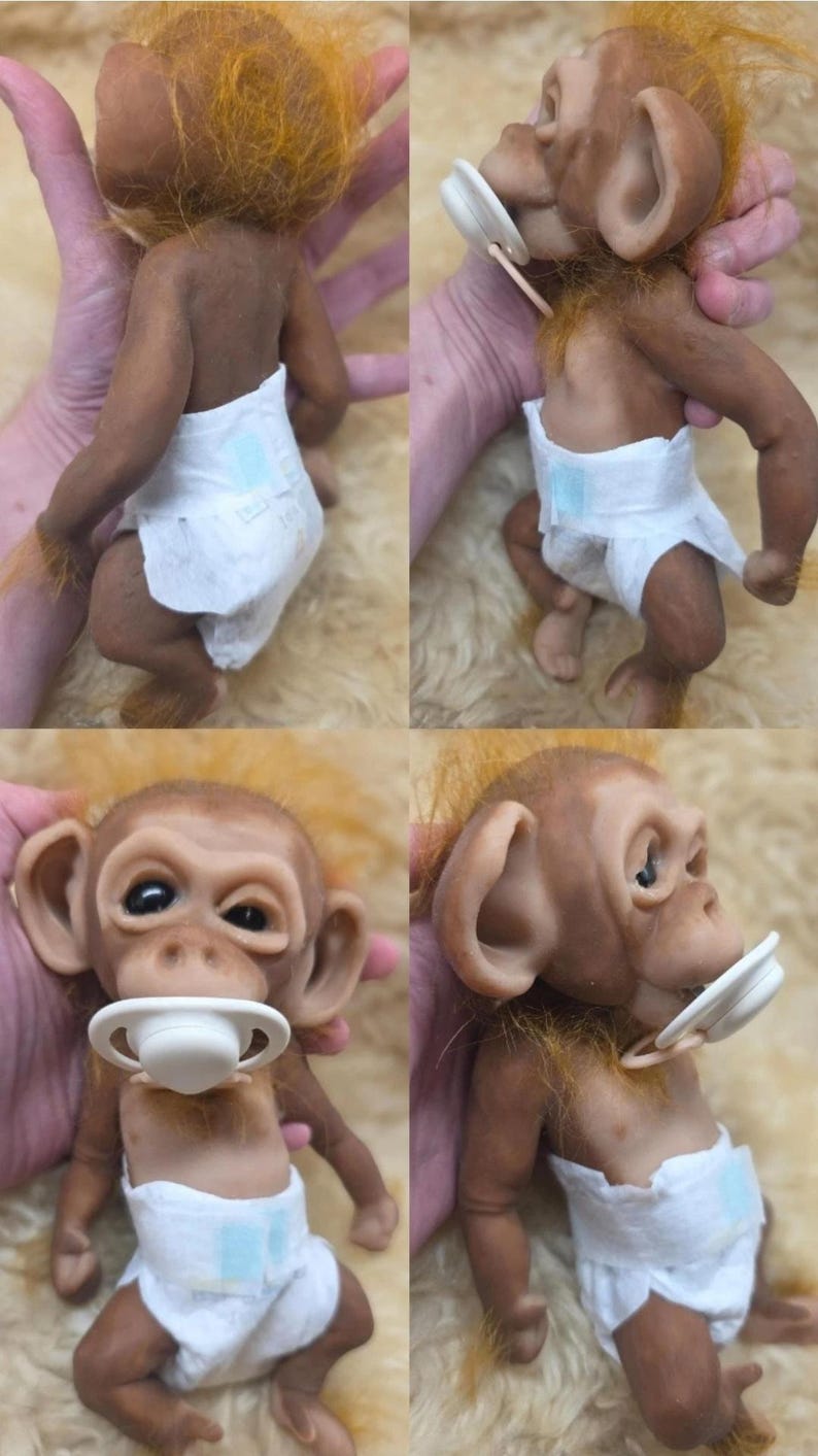May include: A realistic monkey doll with brown skin, orange hair, and large ears. The doll wears a white diaper and has a white pacifier in its mouth. The figure is shown from multiple angles, displaying its textured skin, facial features, and limbs.