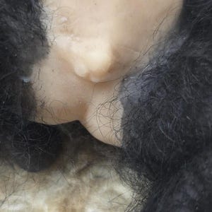 May include: A doll with light-toned skin and a prominent belly button, surrounded by thick, textured black synthetic fur. The doll features realistic skin-like material and dark hair fibers that frame the central torso area in this close-up view.