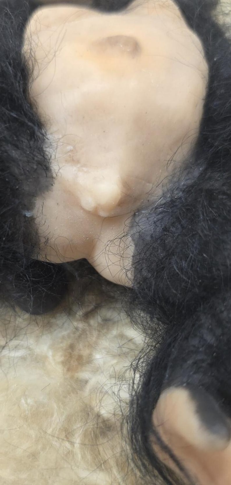May include: A doll with light-toned skin and a prominent belly button, surrounded by thick, textured black synthetic fur. The doll features realistic skin-like material and dark hair fibers that frame the central torso area in this close-up view.