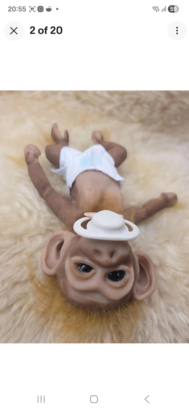 May include: A small monkey figurine with brown skin, dark eyes, and light brown fur around the neck. The monkey is wearing a white diaper and has a white pacifier in its mouth. The figurine is positioned in a lying down orientation.