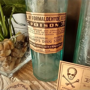 Two antique glass bottles with vintage labels. The bottle on the left has a brown label with the text "OF FORMALDEHYDE, U.S.A. POISON" and "WILLARD'S DRUG STORE". The bottle on the right has a brown label leaning against it which says Arsenic - Poison.