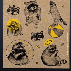 Puede incluir: Una hoja de pegatinas de mapaches en varias poses, con detalles en amarillo. Las pegatinas muestran mapaches de pie, sentados y asom&aacute;ndose a un cubo de basura. El fondo es de color marr&oacute;n claro.
