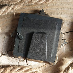 May include: A black picture frame with ornate gold accents. The frame has a black backing and a black stand.