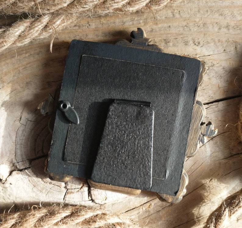 May include: A black picture frame with ornate gold accents. The frame has a black backing and a black stand.