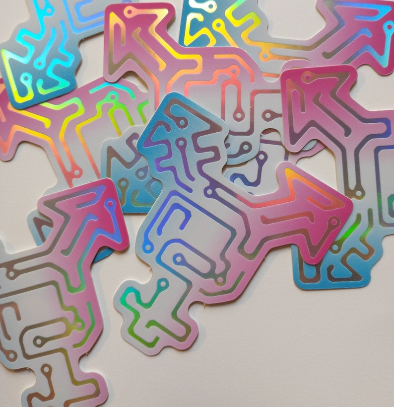 Many identical stickers in the shape of a transgender symbol, with the symbol made of a circuit board pattern. The circuits are holographic rainbow, and the surrounding area is a soft gradient of blue to white to pink, the colors of the trans flag.