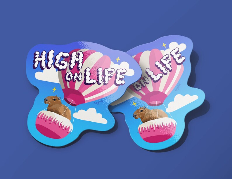 May include: Two stickers featuring a cartoon capybara riding in a hot air balloon. The balloon is pink and white with the words "High on Life" in a bubble font. The stickers are on a blue background.