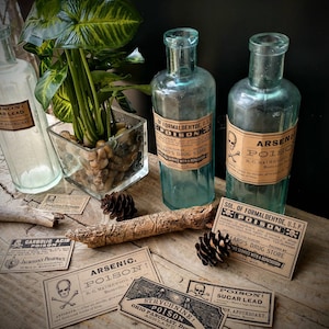 A scene showing antique reproduction label stickers from the Poison Bottle Labels sticker pack. The stickers are printed with blank ink on light brown kraft paper and are rectangular. Formaldehyde and arsenic stickers are shown on antique blue glass pharmacy bottles. Additional stickers such as sugar lead and strychnine are shown lying on a rustic wood surface.