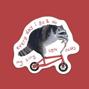 Peut inclure: Un autocollant repr&eacute;sentant un raton laveur sur une trottinette rouge. Le raton laveur est noir, gris et blanc. Le texte sur l'autocollant dit "every day I go & do my silly little tasks" dans un style manuscrit. Le fond est rouge uni.