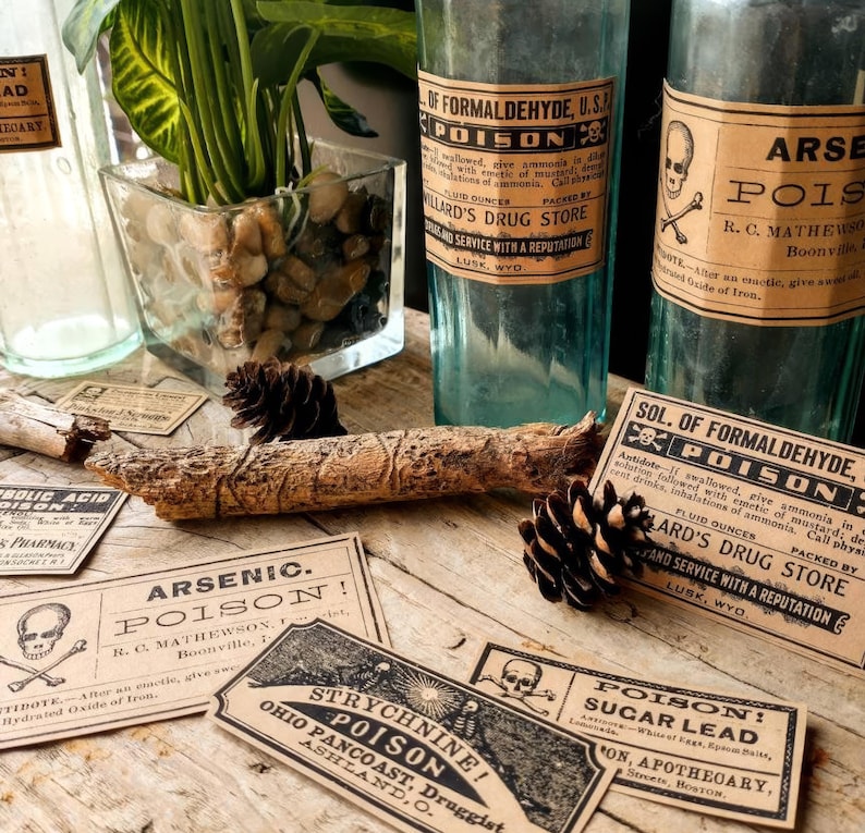 A scene showing antique reproduction label stickers from the Poison Bottle Labels sticker pack. The stickers are printed with blank ink on light brown kraft paper and are rectangular. Formaldehyde and arsenic stickers are shown on antique blue glass pharmacy bottles. Additional stickers such as sugar lead and strychnine are shown lying on a rustic wood surface.