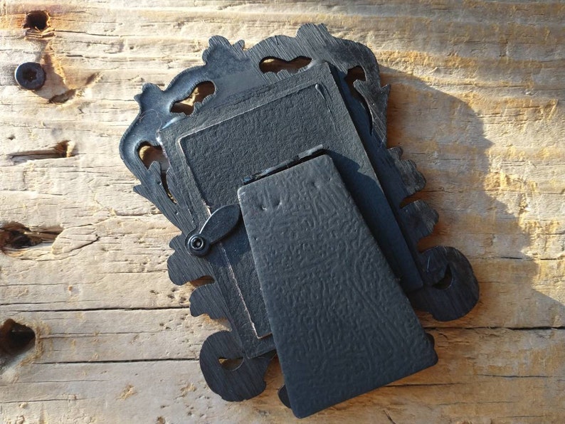 May include: Black ornate picture frame with a stand on the back. The frame is made of wood and has a detailed design.