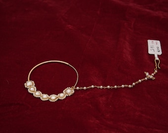 May include: A gold nose ring with a chain and pearl accents. The ring has a circular shape and is decorated with five square-shaped stones. The chain is made of small pearls and is attached to the ring with a small hook. The tag in the image reads "#007 18/1".