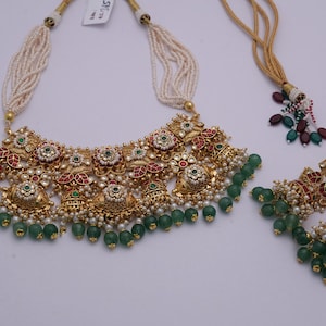 Pu&ograve; includere: Un set di collana e orecchini in oro con perline verdi e bianche, pietre rosse e verdi e intricati motivi floreali.