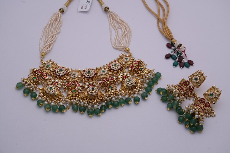 Pu&ograve; includere: Un set di collana e orecchini in oro con perline verdi e bianche, pietre rosse e verdi e intricati motivi floreali.