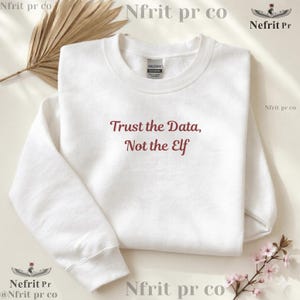 May include: A white crewneck sweatshirt featuring the dark red embroidered text Trust the Data, Not the Elf centered on the chest. The garment has long sleeves, a ribbed collar, and a standard fit, presented with a clean and simple aesthetic.