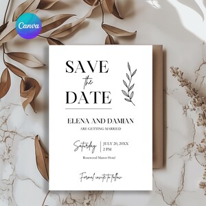 Op de afbeelding: Een witte "Save the Date" kaart met zwarte tekst, met de namen Elena en Damian en huwelijksdetails. De kaart heeft een bloemenontwerp en staat tegen een marmeren achtergrond met gedroogde bladeren.