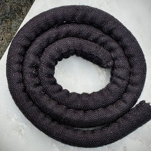 May include: A black, coiled, fabric rope. The rope is made of a woven material and is approximately 1 inch in diameter.
