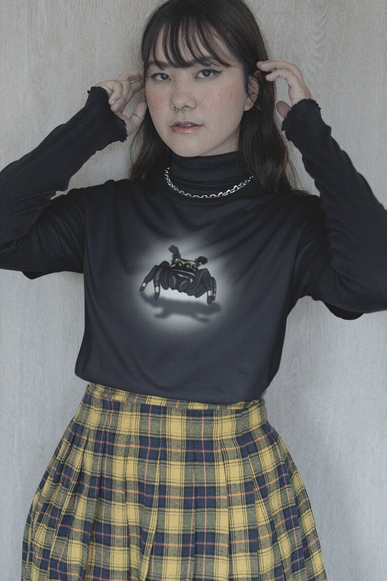 Może przedstawiać: Czarny, długorękawny t-shirt z nadrukiem pająka z przodu. Koszulka jest połączona z ż&oacute;łto-czarną sp&oacute;dnicą w kratę.