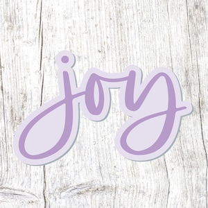 May include: Purple cursive word "joy" on a white wood background.