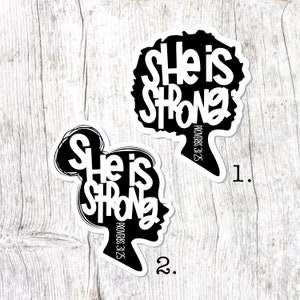 May include: Two black and white stickers with the text "She is Strong" and the Bible verse "Proverbs 3:25". The stickers feature a silhouette of a woman's head with an afro hairstyle and a woman's head with a bun.