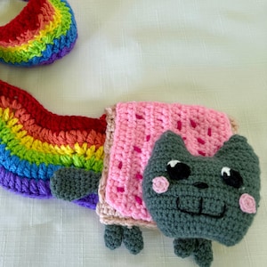 Puede incluir: Bufanda Nyan Cat de ganchillo, con cola arcoíris y cuerpo rosa de Pop-Tart. La cara del gato es gris con ojos negros, mejillas rosas y boca sonriente. Un accesorio divertido y colorido hecho de hilo suave.