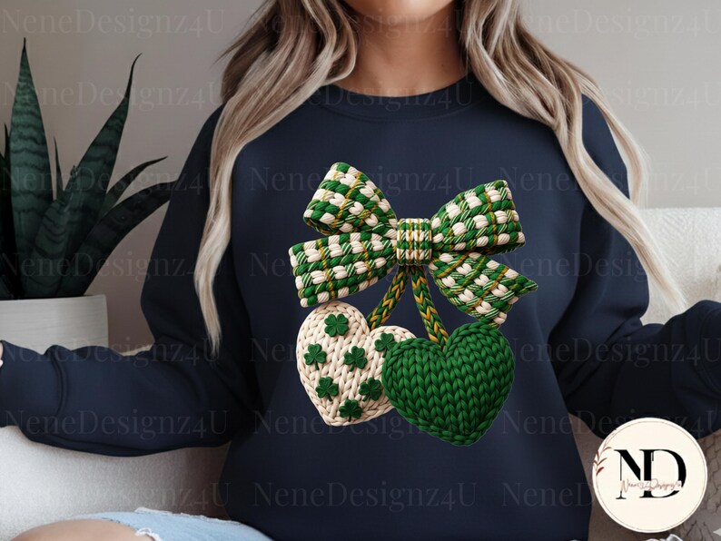 May include: Navy blue sweatshirt featuring a green and white bow and two heart-shaped ornaments. One heart is green, the other is white with green shamrocks. The design is a knitted style, perfect for St. Patrick's Day.