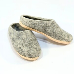 Puede incluir: Un par de zapatillas sin cordones hechas de lana afieltrada de color gris jaspeado. Las zapatillas presentan una punta redondeada, una abertura baja y una suela plana de color beige claro cosida por el borde, con un diseño sencillo.