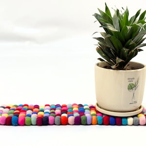 Op de afbeelding: Een kleurrijke vilt potmat met een gepotte plant in een witte keramische pot met de tekst "Simple View" aan de zijkant. De plant heeft groene bladeren.