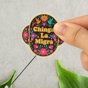 May include: A badge reel with a floral design and the text "Chinga La Migra". The badge reel has a clear plastic clip and a black retractable cord. The design includes colorful flowers and birds.