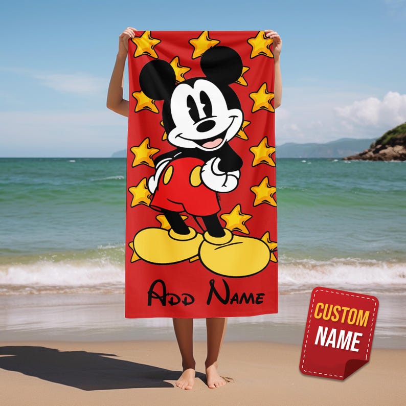 May include: A rectangular beach towel with a vibrant red background featuring a large graphic of Mickey Mouse wearing red shorts and yellow shoes. The design includes scattered yellow stars and the black text Add Name at the bottom.