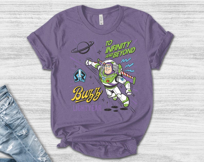 May include: A purple short-sleeve t-shirt featuring a graphic of Buzz Lightyear in a flying pose. The design includes the text "TO INFINITY AND BEYOND" in green, "Buzz" in yellow, and "LIGHTYEAR" in purple, along with a planet and star icons.