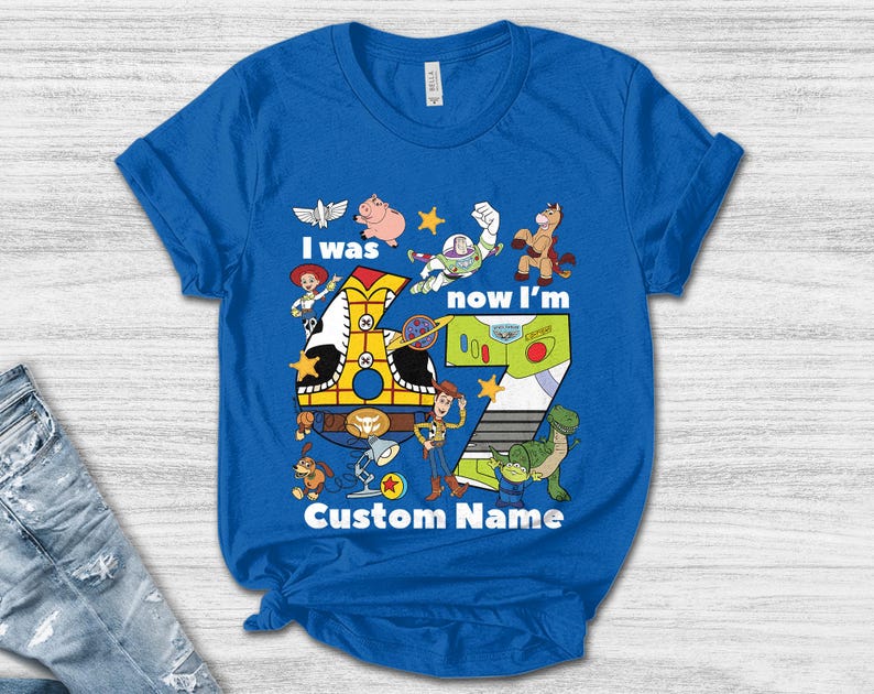 May include: Blue t-shirt featuring a colorful graphic with characters and the number 7 from the animated movie. The text reads "I was now I'm" and "Custom Name".