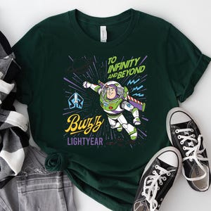 May include: A dark green t-shirt featuring a graphic of Buzz Lightyear in flight. The design includes the text "TO INFINITY AND BEYOND" in green, "Buzz" in yellow script, and "LIGHTYEAR" in purple, set against a background of stars and lines.