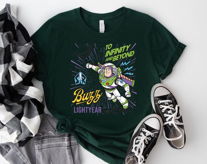 May include: A dark green t-shirt featuring a graphic of Buzz Lightyear in flight. The design includes the text "TO INFINITY AND BEYOND" in green, "Buzz" in yellow script, and "LIGHTYEAR" in purple, set against a background of stars and lines.