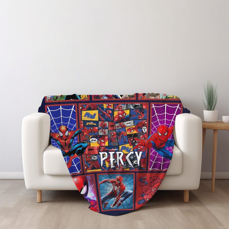 May include: A Spider-Man themed blanket featuring a collage of comic book panels and illustrations. The blanket is primarily red, blue, and white, with the name "PERCY" displayed prominently. The blanket is draped over a white sofa.