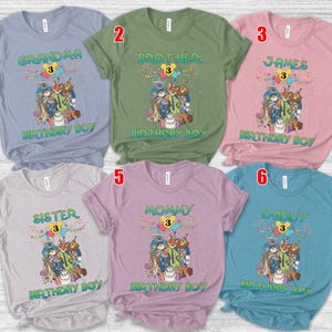 May include: Six short-sleeved crew neck t-shirts in light blue, olive green, pink, light gray, lavender, and teal. Each shirt features a graphic of animated animal characters, a birthday cake, balloons, and the text "BIRTHDAY BOY" with a number 3.
