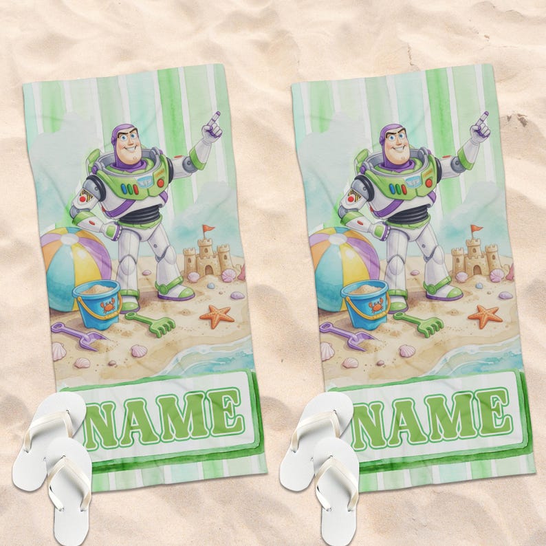 May include: Two rectangular beach towels featuring a cartoon space ranger character in a white, green, and purple suit. The design includes a sandcastle, a beach ball, a blue bucket, and the word NAME in green letters, paired with white flip-flops.