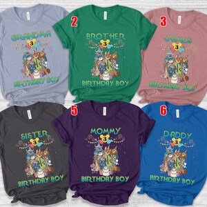 May include: Six short-sleeved crew neck t-shirts in light blue, green, mauve, dark gray, purple, and royal blue. Each shirt features a graphic of animated animal characters, a birthday cake, and the text "BIRTHDAY BOY" with a number 3.