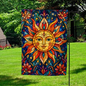 May include: A colorful garden flag featuring a stained-glass style sun design. The sun has a smiling face with blue eyes, surrounded by orange, yellow, and red rays. The background is a mosaic of blue, purple, and green, with floral accents.