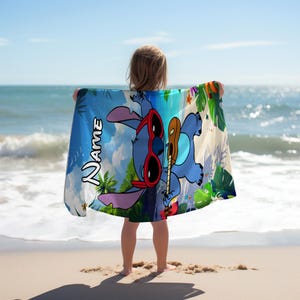 May include: A rectangular beach towel featuring a blue cartoon character wearing red sunglasses and holding a brown ukulele. The design includes tropical green leaves, colorful flowers, and the word NAME printed in a bold white font on the left side.
