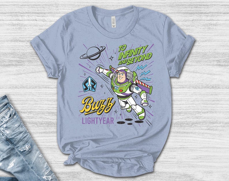 May include: A light blue t-shirt featuring a graphic of Buzz Lightyear in a flying pose. The design includes the text "TO INFINITY AND BEYOND", "Buzz", and "LIGHTYEAR" in green, yellow, and purple, along with a planet icon and a space ranger emblem.